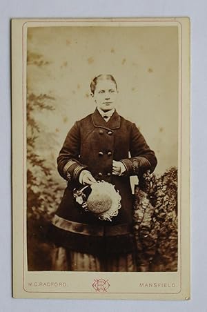 Carte De Visite Photograph. Studio Portrait of a Young Woman Wearing a Coat & Holding a Hat.