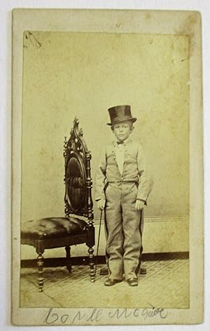 CARTE DE VISITE OF UNKNOWN YOUNG DWARF, POSSIBLY A PERFORMER, STANDING NEXT TO AN ORNATE CHAIR WH...