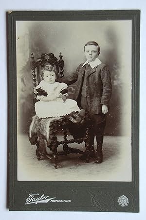 Cabinet Photograph: Studio Portrait of a Young Boy with His Sister Seated on a Chair.