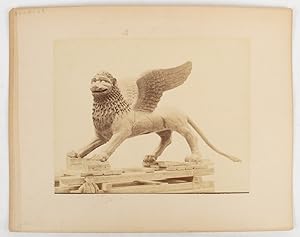 [Sculpture or cast of a griffin on a wooden pallet with a small boy in the foreground.]