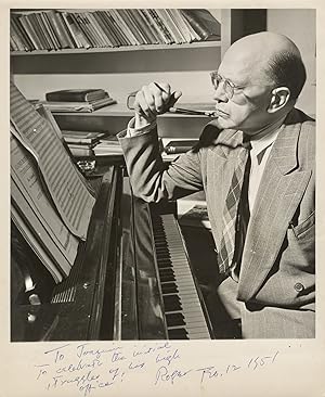 Photograph of Sessions seated at the piano, pen in hand, with sheets of manuscript paper before h...