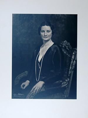 Halbportrait nach halblinks in schwarzem Kleid mit Perlenkette auf einem Sessel. Photographischer...