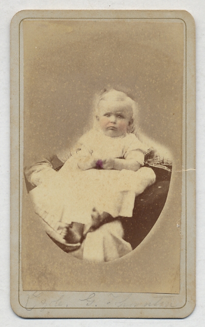[Photograph]: Infant In White Dress sitting on a cushion, cheeks highlighted with pink, identified in pencil in lower margin as "Lzole. G. Thornton"