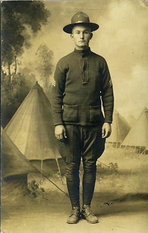 Postcard of World War I soldier, a studio shot in front a background scene ot conical pitched tents