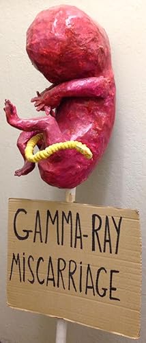 Gamma-ray miscarriage [protest sign with papier maché sculpture in form of a fetus]