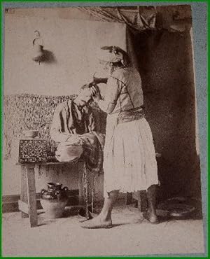 Bild des Verkufers fr Grande photographie anciennes originale (Vers 1880).Tirage albumin d'poque mont sur carton bleu-vert reprsentant un Coiffeur arabe zum Verkauf von JOIE DE LIRE