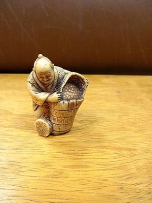 Netsuke: Ein Mann bei der Weinlese schüttet die Trauben in ein Gefäß. Figur um 1900, unsigniert. ...