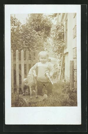 Ansichtskarte Kleinkind steht im Garten neben seinem Schaukelpferd