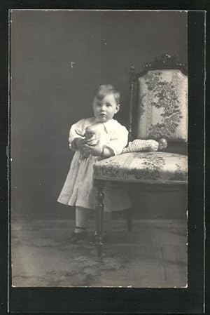 Foto-Ansichtskarte Kleines Mädchen mit Puppen lehnt am Stuhl