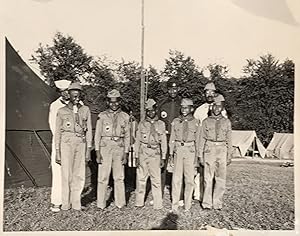 Bild des Verkufers fr FIVE 12-15 YEAR OLD AFRICAN-AMERICAN BOY SCOUTS, in full uniform (khakis, side caps, kerchiefs, lanyards, official badges, etc.), along with three older African-American leaders, also in full uniform, as pictured in a large format photograph, 8 x 10 inches, standing in a campground, with tents and a stand of trees in the background zum Verkauf von Bartleby's Books, ABAA