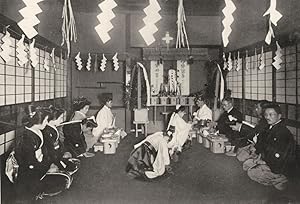 Seller image for A Modern Shinto marriage service performed in a house - In the alcove is erected an altar with offerings to the Japanese creator and creatrix. The room is hung with the sacred gohei, paper streamers to ward off evil and to purify all present. The bridegroom is in the act of receiving the consecrated wine poured into a tiny porcelain cup which he holds; near the improvised altar sit the two priests, robed in white for sale by Antiqua Print Gallery