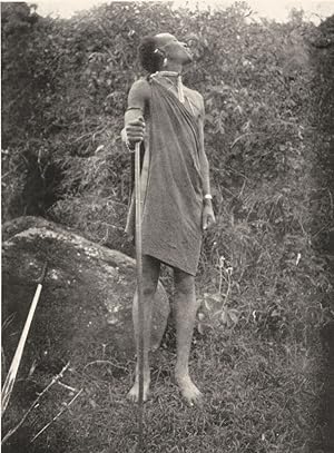 Seller image for A Dorobo spitting as a sign of devotion - A Dorobo before saying his morning prayer spits towards the rising sun. Whilst engaged in prayer he lays aside his sword. The Dorobos are supposed to have great influence over the rain, and to prevent it falling whistle and shake their swords at the sky for sale by Antiqua Print Gallery