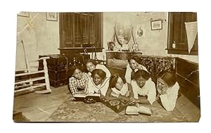 Imagen del vendedor de Photo on Postcard of Seven Young African American Women Lying on the Floor while Studying jointly out of two textbooks. A felt Bennett Pennant Hangs on a Closed Shutter a la venta por McBlain Books, ABAA