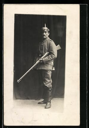 Foto-Ansichtskarte preussishcer Soldat in Feldgrau Uniform mit Pickelhaube und Gewehr, Ledergamas...