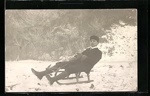 Foto-Ansichtskarte Junger Mann auf einem Schlitten im Schnee